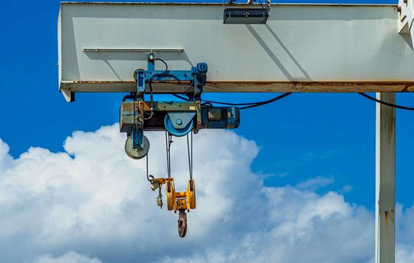 Industrial gantry crane with hooks against a blue sky.