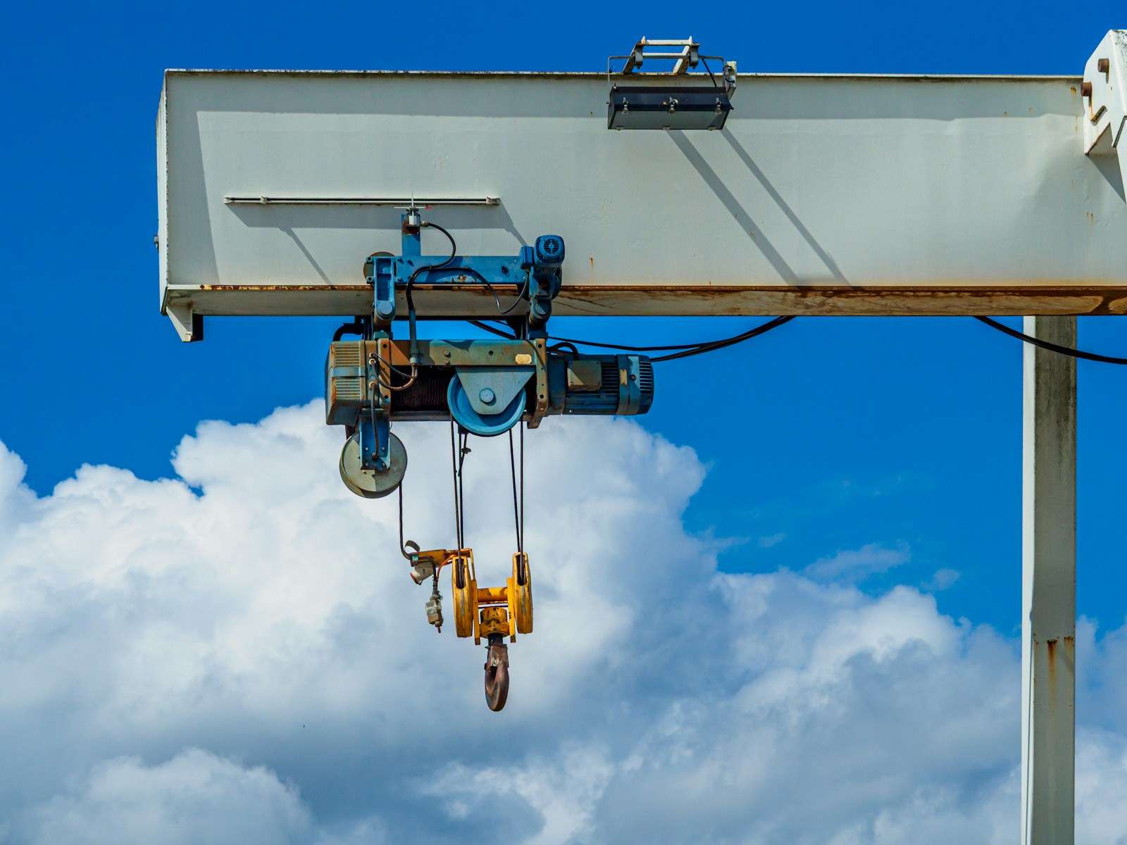 Industrial gantry crane with hooks against a blue sky.