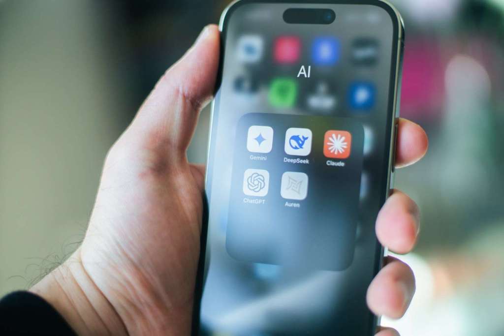 A hand holds a smartphone with various apps.